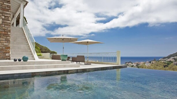 Una piscina infinita con vistas despejadas al mar, mobiliario exterior y una escalera que conduce a una terraza.