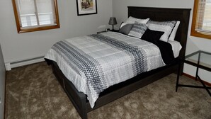 A bedroom with a bed, a nightstand, a lamp, a framed picture on the wall, and two windows with blinds. - Quaint updated apartment overlooking the Bay (Washburn)