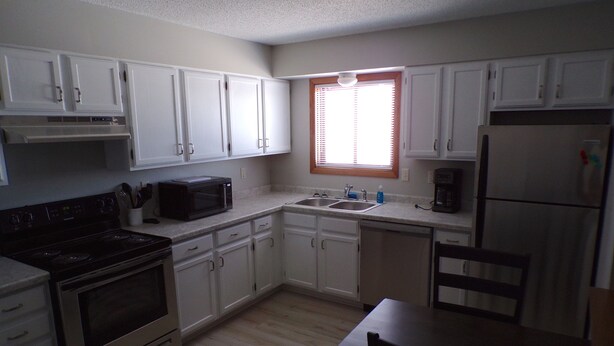 A kitchen with white cabinets, a stove, microwave, sink, and a refrigerator. - Quaint updated apartment overlooking the Bay (Washburn)