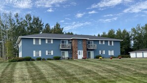A two-story blue building with a brick entrance, a balcony on the second floor, and a well-maintained lawn. - Quaint updated apartment overlooking the Bay (Washburn)