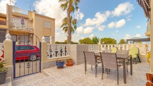 An outdoor patio with a patterned tile floor, a dining table with chairs, a red car parked in front of a gate, and a palm tree in the background. - 2 bedroom gorgeous apartment in Torrevieja (Torrevieja)