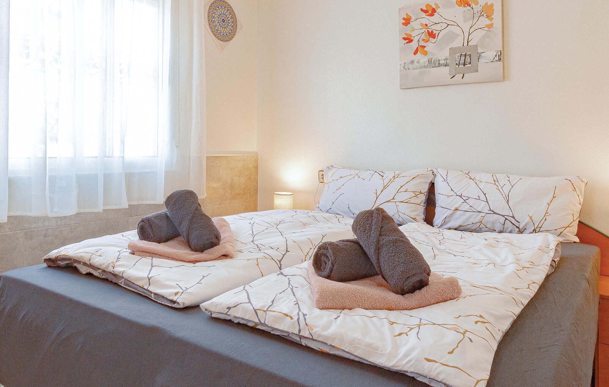 Un dormitorio con dos camas, cada una con un par de toallas, una mesita de noche, una lámpara y una obra de arte en la pared.