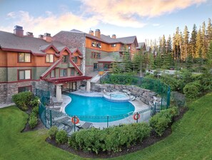 Propiedad residencial con piscina, fachada de piedra y madera, y jardín ajardinado.