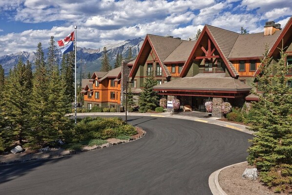 Un albergue con una visible bandera canadiense, rodeado de montañas y pinos.