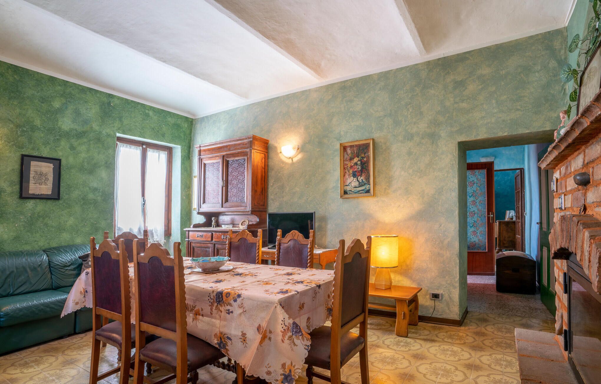 Un comedor con una mesa dispuesta para cuatro personas, rodeada de sillas de madera, un aparador de madera y un cuadro en la pared.
