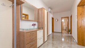 A hallway with a wooden cabinet, a glass-top desk, and a mirror. There is a potted plant and a door leading to a bathroom. - Awesome apartment in Gornje Rastane (Gornje Rastane)