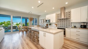 A modern kitchen with a large island, white cabinetry, and a view to the outside. - Canal Front with Cabana Club Privileges! Paddleboards, Bikes, Kayak in KCB! (Key Colony Beach)