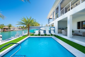 Un espace piscine moderne avec une piscine à l’eau d’un bleu limpide, des chaises longues blanches et un bâtiment blanc doté de balcons.