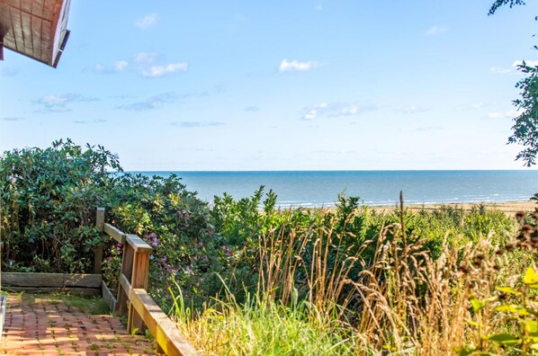 A coastal view with a wooden deck and a brick pathway leading to a beach. - Nice home in Frederikshavn with WiFi (Frederikshavn)
