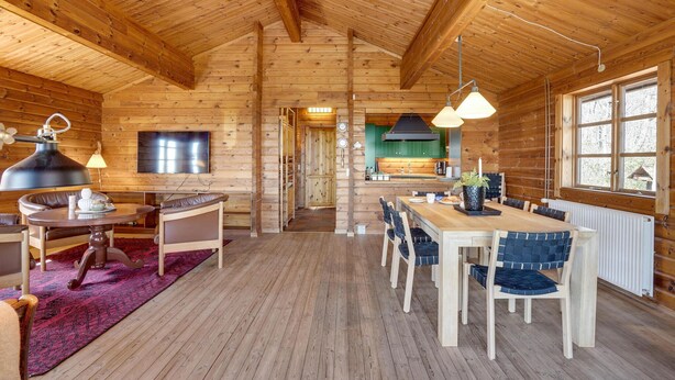 Un acogedor interior de cabaña de madera con comedor, cocina y televisor montado en la pared.