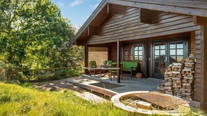 Una cabaña de madera con terraza, mobiliario exterior y una fogata.