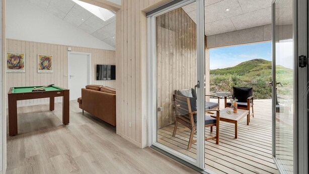 Ein modernes Wohnzimmer mit Billardtisch, einer Couch und einer Glasschiebetür, die auf eine Terrasse mit Blick auf die Hügel führt.