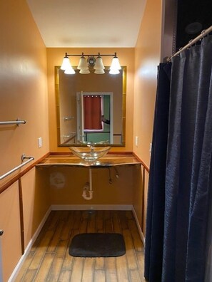 A bathroom with a glass sink, wooden floor, and a mirror above the sink. - Aloha Beach Club Resort (Oscoda)