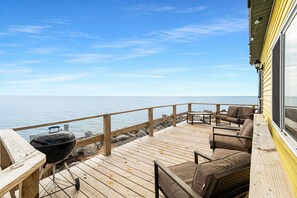 Una terraza de madera con una parrilla, asientos y vistas al agua.