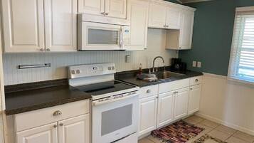 A kitchen with white cabinets, a microwave, an oven, a sink, and a patterned rug.