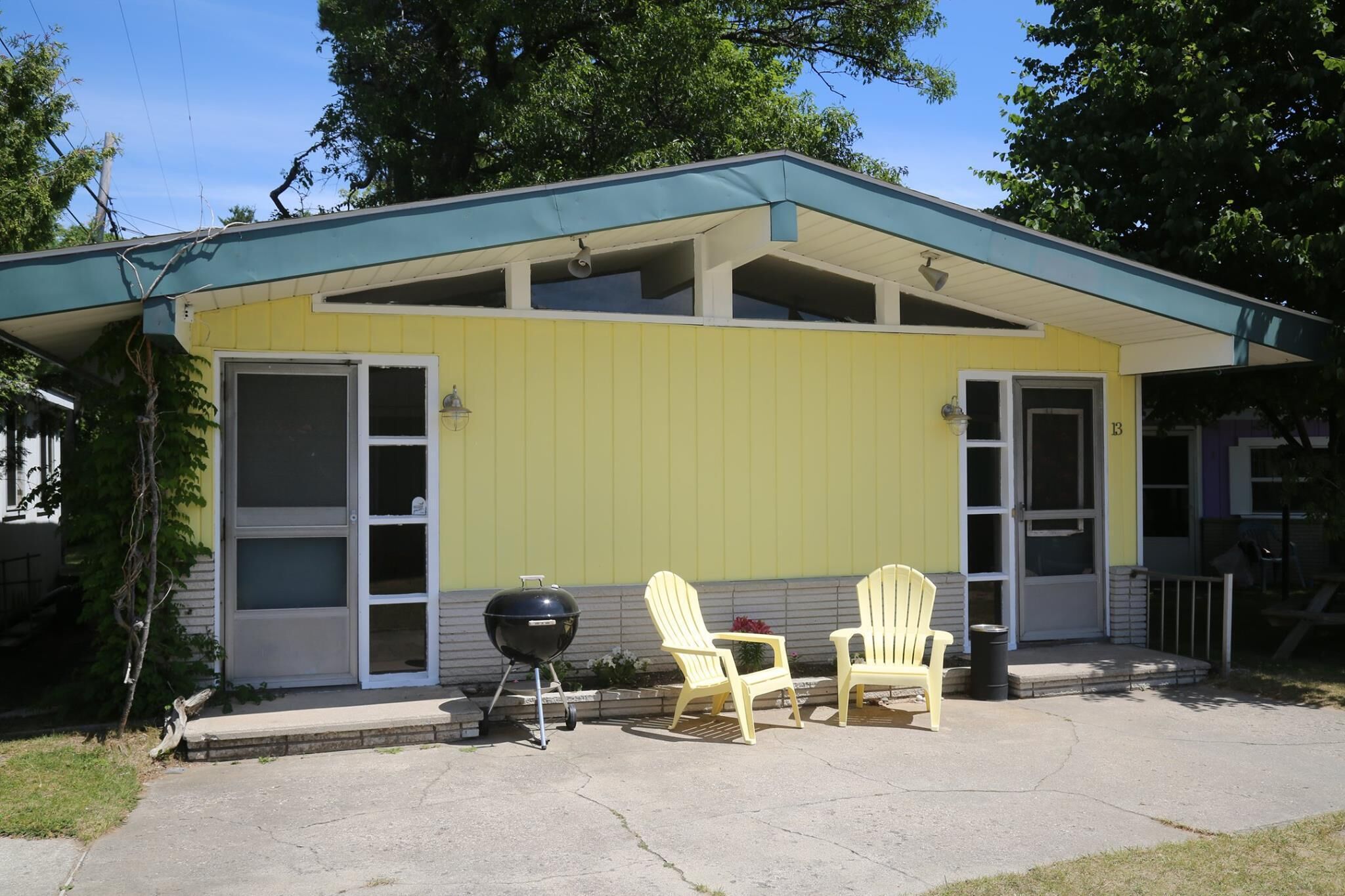 Un bâtiment jaune doté d’un porche abrité, de deux fauteuils Adirondack et d’un barbecue.