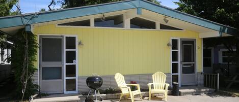 Un bâtiment jaune doté d’un porche abrité, de deux fauteuils Adirondack et d’un barbecue.
