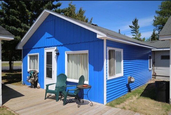 A blue cabin with a porch, two green Adirondack chairs, and a small table. - Aloha Beach Club Resort (Oscoda)
