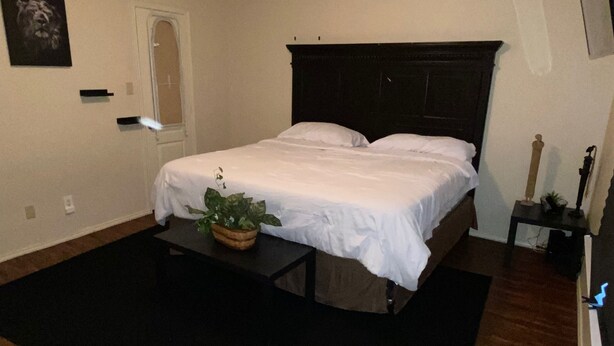 Quarto com uma cama de casal, uma mesinha de cabeceira com uma planta, uma pequena mesa e um espelho na parede.
