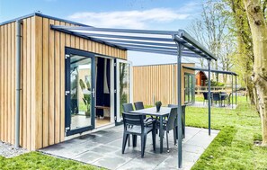 A modern outdoor patio with a wooden deck, a glass door entrance, and a covered seating area with chairs and a table.