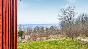 Une vue depuis une fenêtre donnant sur une étendue d’eau, avec une zone herbeuse et des arbres sans feuilles au premier plan.