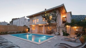 Una casa de dos pisos con piscina, mobiliario exterior y fachada de piedra.