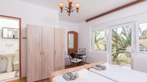 Un dormitorio con un armario de madera, una pequeña mesa con sillas, una cama con toallas y una ventana con vistas a zonas verdes.