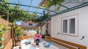 Un espacio exterior para comer con una mesa preparada para cuatro personas, rodeado por una valla de madera y una pérgola cubierta de hiedra.