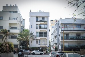 Un immeuble résidentiel à plusieurs étages, doté de balcons, avec des voitures garées et un palmier.