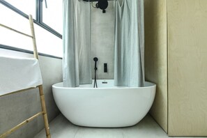 Ein modernes Badezimmer mit einer freistehenden Badewanne, einer Bambusleiter und einem Fenster mit Vorhängen.