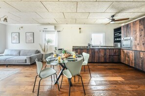 Eine moderne Küche mit Holzschränken, ein Essbereich mit einem runden Tisch und Stühlen sowie ein graues Sofa in einem geräumigen Wohnzimmer.