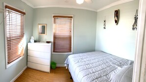 A bedroom with a bed, dresser, two windows with blinds, a mirror, and a green trash bin. - Hop, skip, jump to the beach! (Point Pleasant Beach)