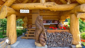 A wooden sauna structure with a sign, a bear sculpture, and a stack of firewood. - Amazing home in Hlevci with sauna (Hlevci)