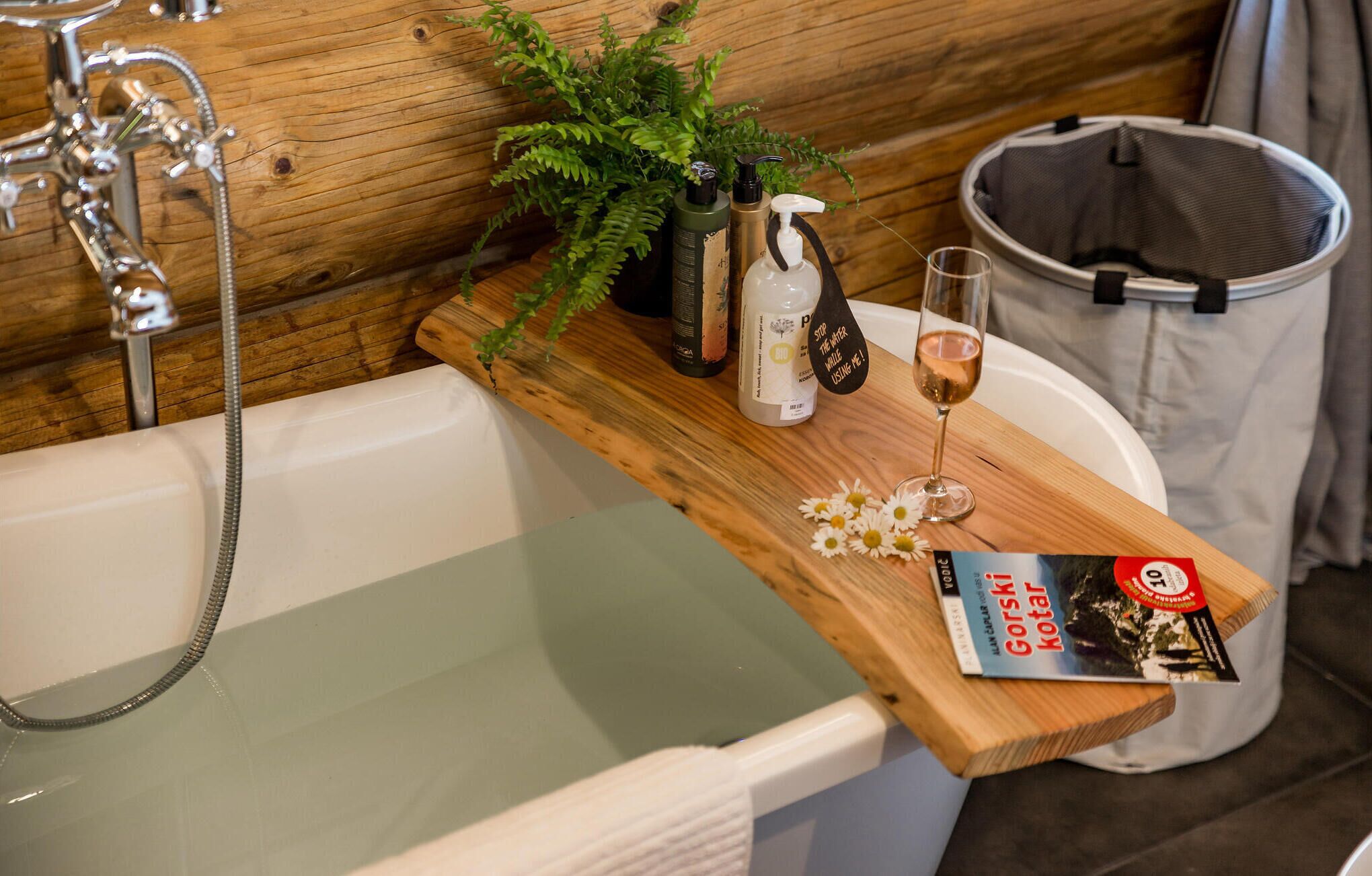A bathroom with a wooden vanity, a bathtub, a shower, and a trash bin.