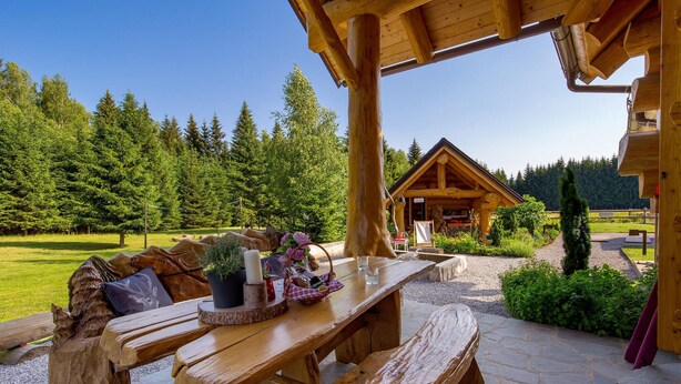 A wooden picnic table with benches, a wooden cabin in the background, and a forested landscape. - Amazing home in Hlevci with sauna (Hlevci)