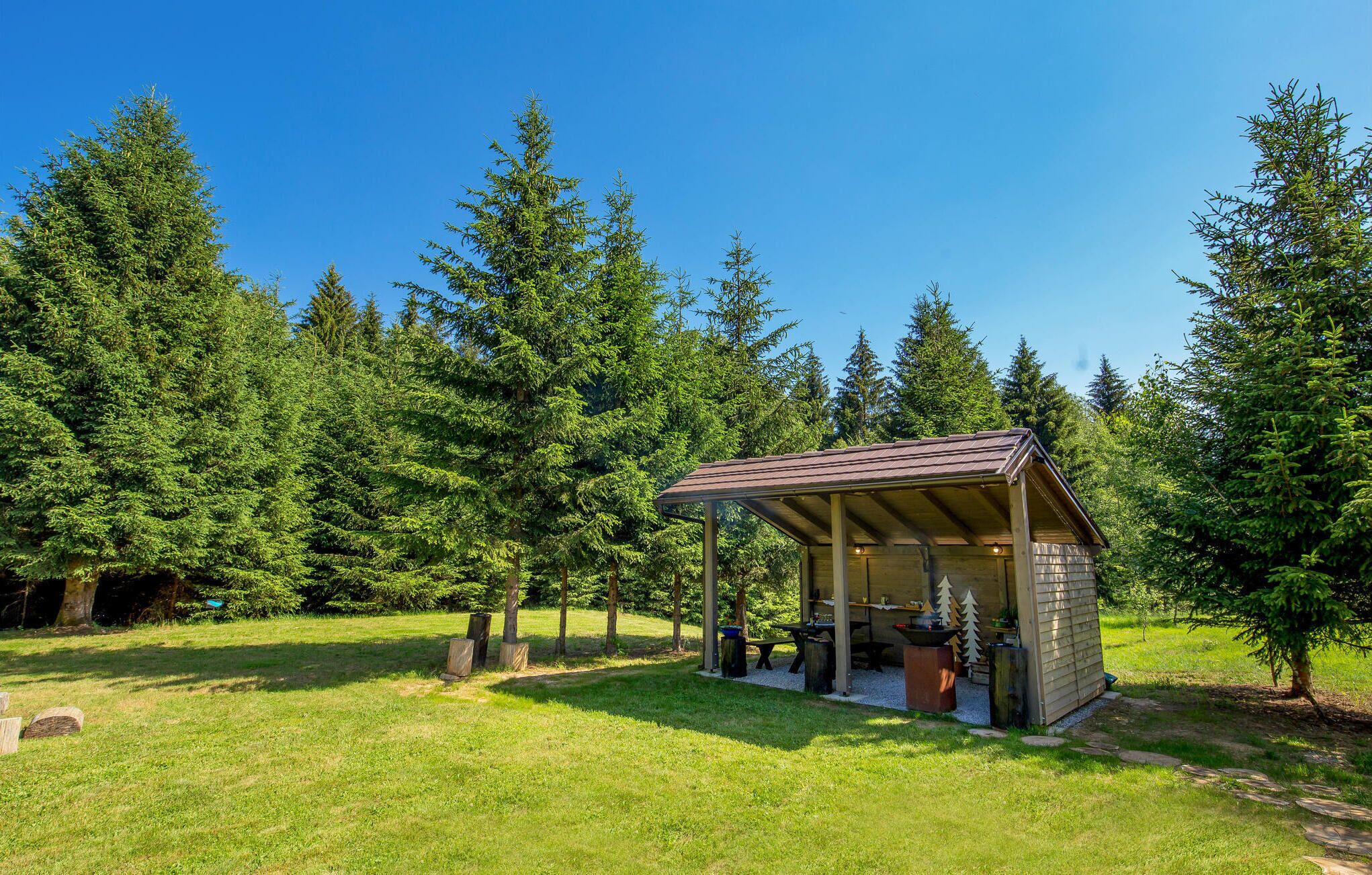 Eine kleine Holzhütte mit Dach, umgeben von einer grünen Wiese und hohen Bäumen.