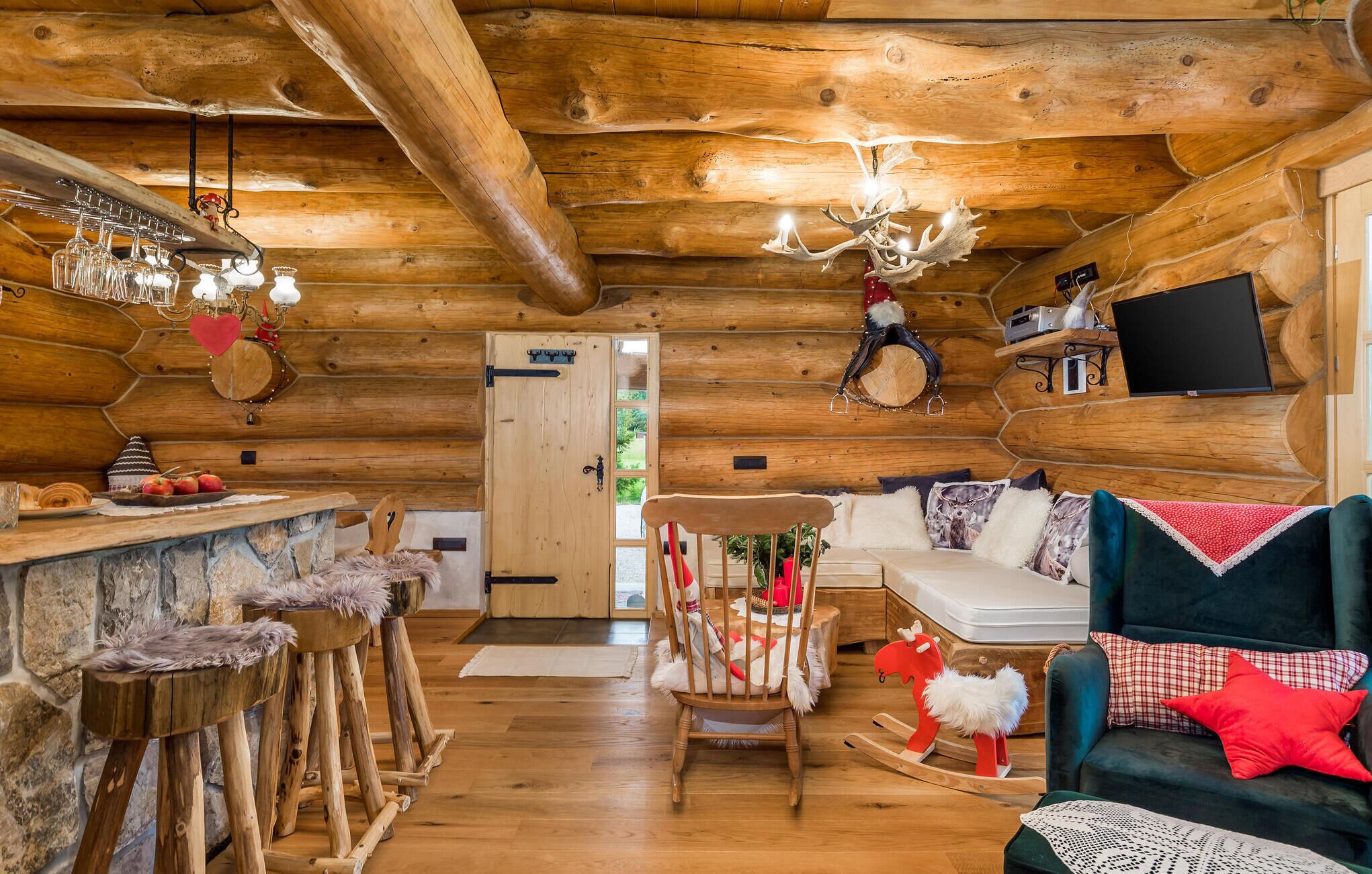 Interior acolhedor de uma cabana de madeira, com área de jantar em madeira, sofá e televisão fixada na parede.