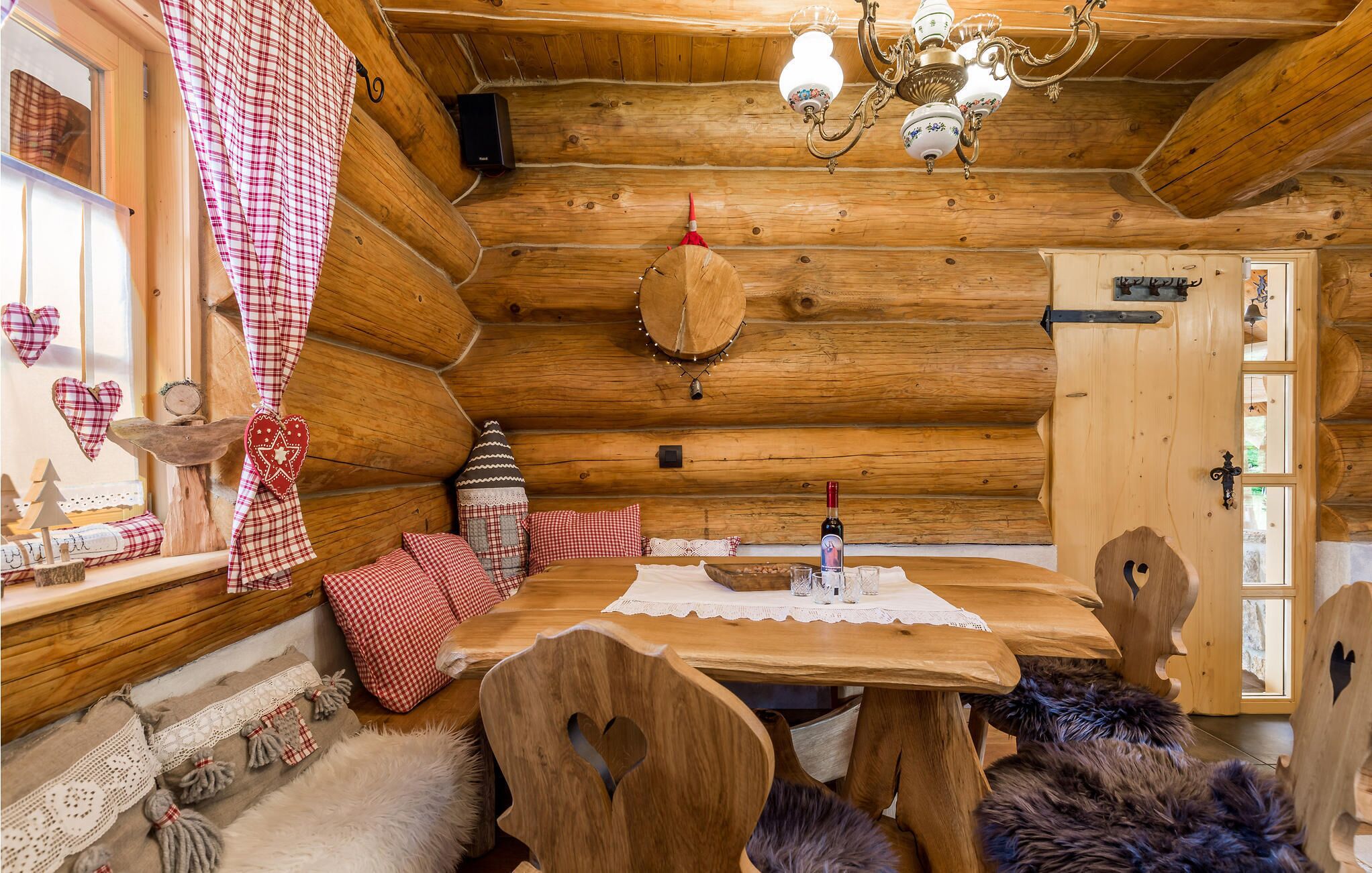 A cozy log cabin interior with a wooden dining table, chairs, and a chandelier.
