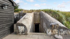 A stone entrance with a metal door, a wooden building on the left, and a grassy area in the background.