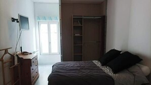 Un dormitorio con una cama, un aparador, un televisor sobre un mueble bajo y un armario.