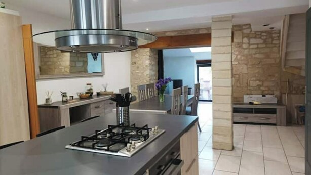Una cocina moderna con una isla central, una campana extractora de acero inoxidable y una pared de acento de piedra.