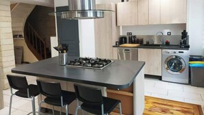 Una cocina moderna con una isla central, taburetes de bar, lavadora integrada y una campana extractora de acero inoxidable.