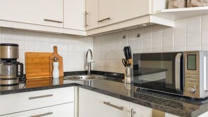 Una cocina moderna con armarios blancos, encimera de granito, cafetera, microondas y tabla de cortar de madera.