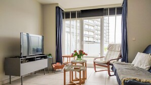 Una sala de estar moderna con un televisor de pantalla plana, una mesita redonda con un florero, un sofá y una silla.