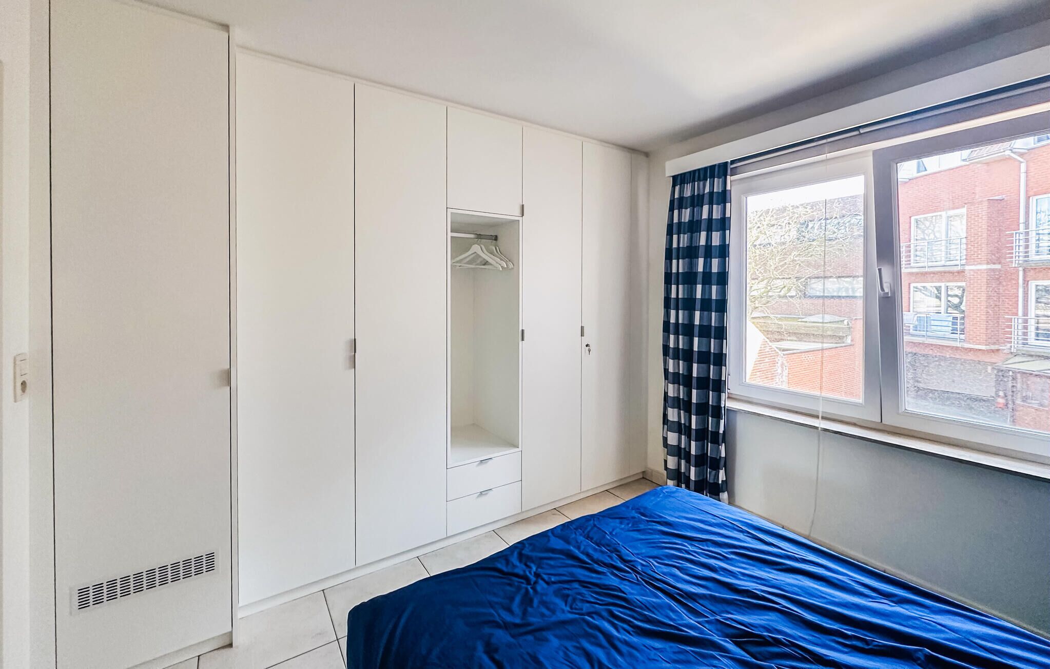 Un dormitorio con cama, armario y ventana con cortinas.