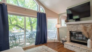 A living room with a fireplace, a TV mounted above it, and a large window with curtains. - Spacious Family Lake House In Quiet Cove | 45 (Sunrise Beach)