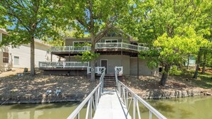 A dock leading to a house with a balcony, surrounded by trees and a body of water. - Spacious Family Lake House In Quiet Cove | 45 (Sunrise Beach)