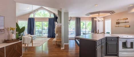 A spacious kitchen with a central island, a dining area with a view, and a living room with a large window.