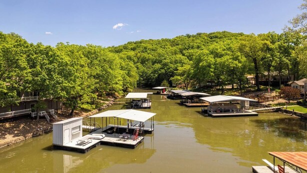A riverside area with docked boats and covered structures, surrounded by lush green trees. - Spacious Family Lake House In Quiet Cove | 45 (Sunrise Beach)