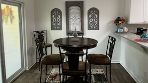 Un comedor con una mesa redonda, cuatro sillas, decoración en la pared y una lámpara colgante.